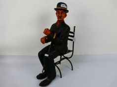 A figure depicting Charlie Chaplin in a seated pose with metal chair, approximately 57 cm (h). [2].