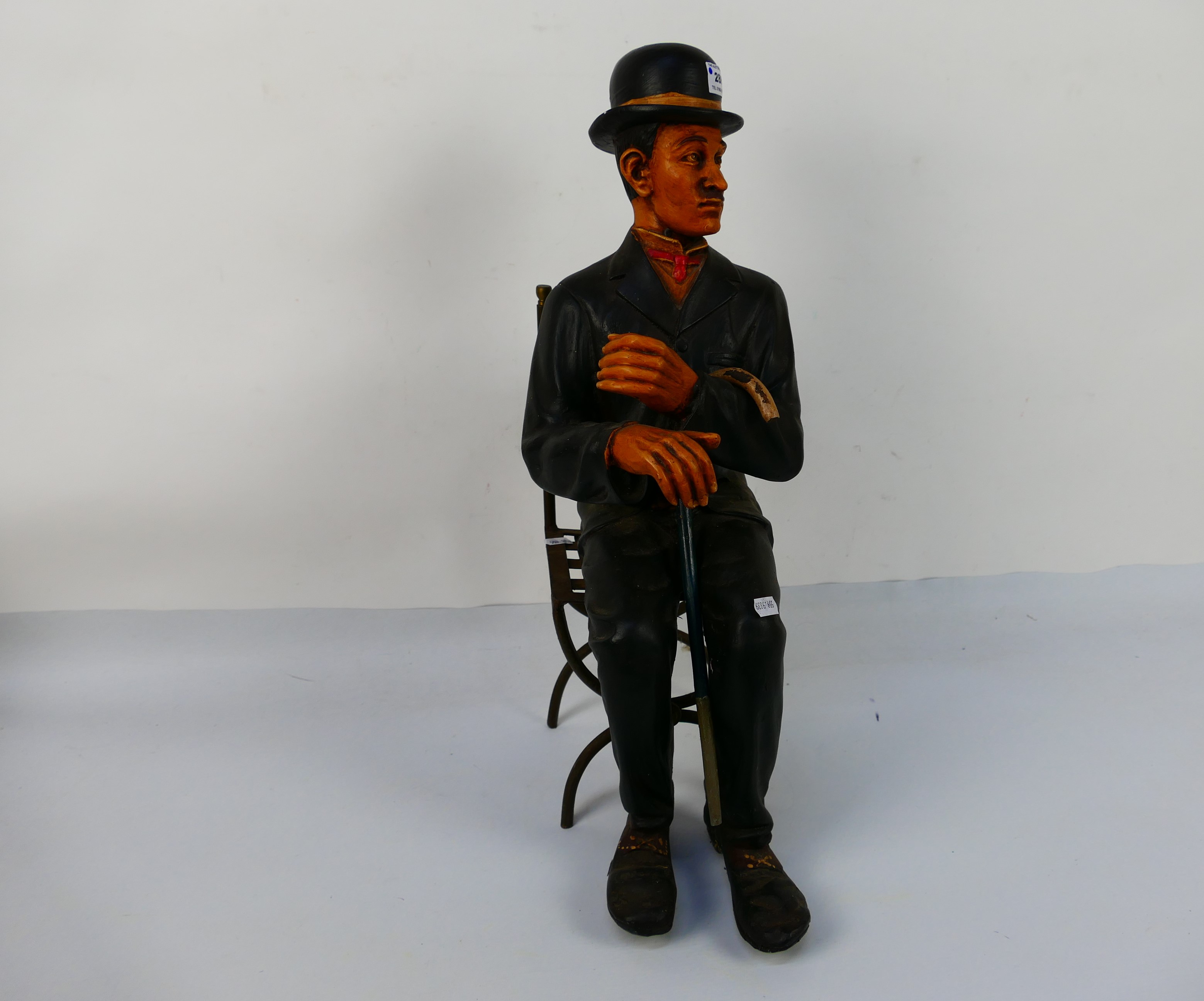 A figure depicting Charlie Chaplin in a seated pose with metal chair, approximately 57 cm (h). [2]. - Image 2 of 3