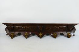 An oak and brass wall mountable coat rack decorated with three carved lion masks and foliate