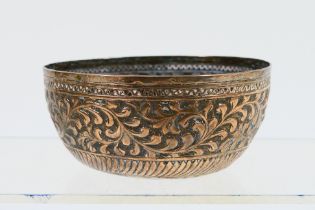 An Indonesian white metal bowl with foliate scroll repousse decoration to the body and crossed Kris