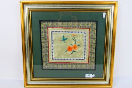 A Chinese embroidery on silk depicting flowers and an insect, framed under glass,
