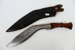 A vintage kukri with 30 cm (l) blade, wooden hilt and brass chapri, housed in leather scabbard.