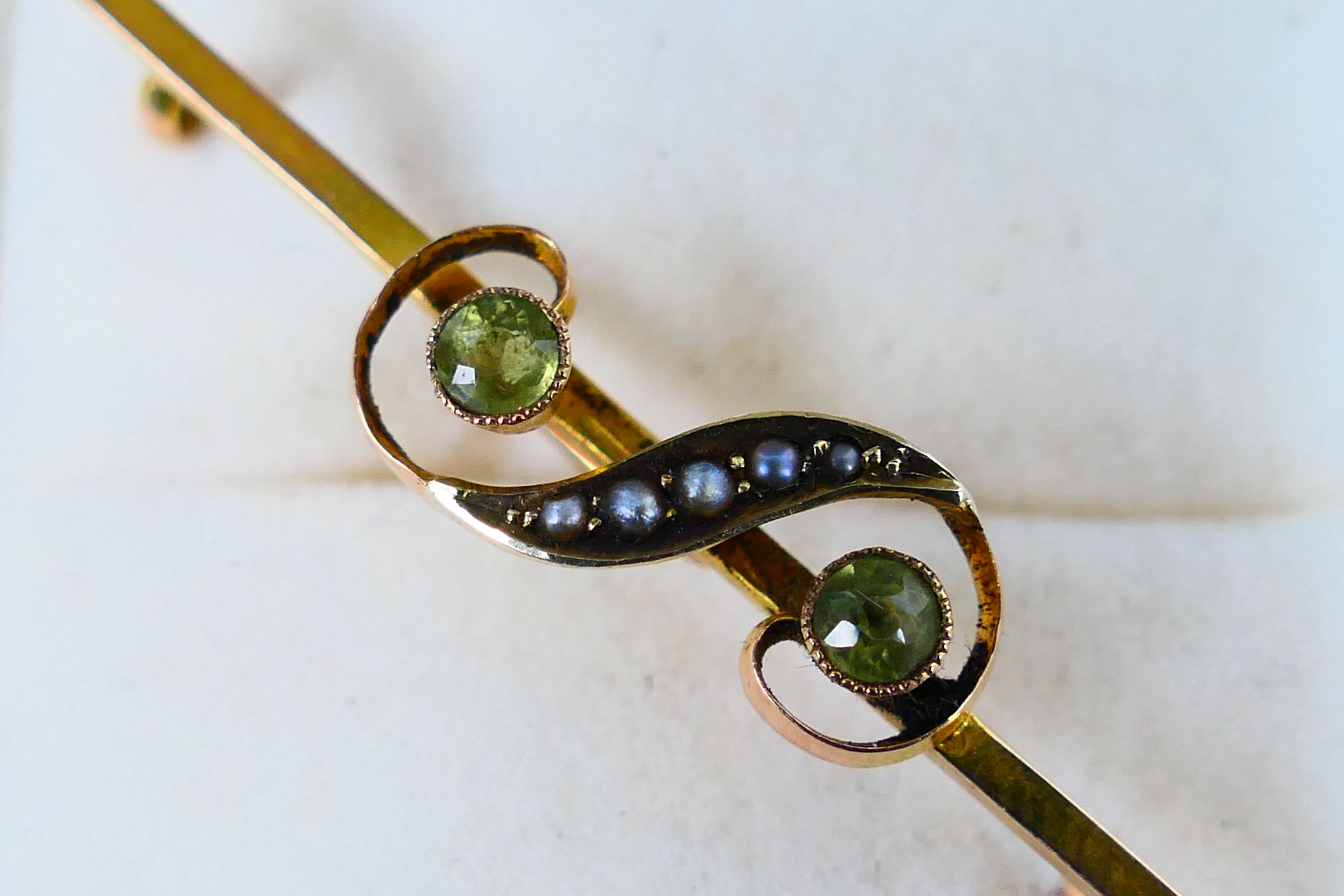 A 9ct gold bar brooch set with peridot and seed pearl in the form of a gruppetto or turn, 5 cm (l), - Image 2 of 3