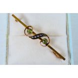 A 9ct gold bar brooch set with peridot and seed pearl in the form of a gruppetto or turn, 5 cm (l),