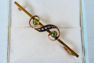 A 9ct gold bar brooch set with peridot and seed pearl in the form of a gruppetto or turn, 5 cm (l),