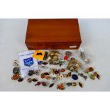 A polished wood box containing a quantity of enamelled pin badges and charms including several with