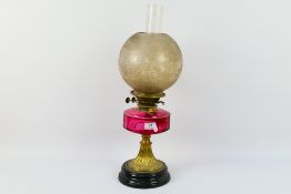 A Victorian brass oil lamp with cranberry glass font, font 15 cm (d),