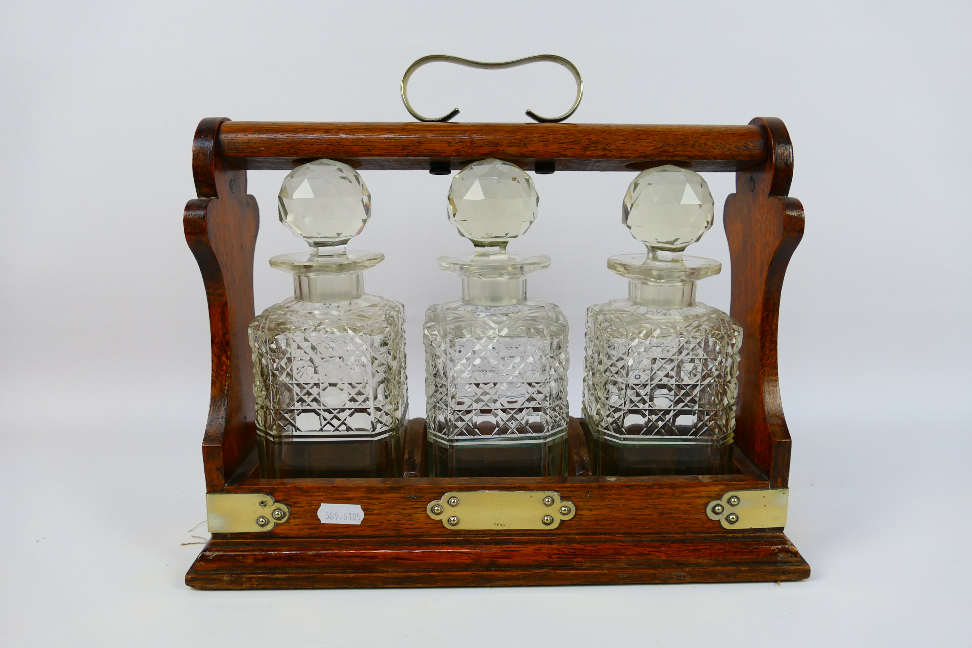 A three decanter oak tantalus with plated mounts, no maker's mark visible.