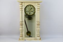 A white painted wall clock, Roman numerals to a white dial, with key and pendulum.