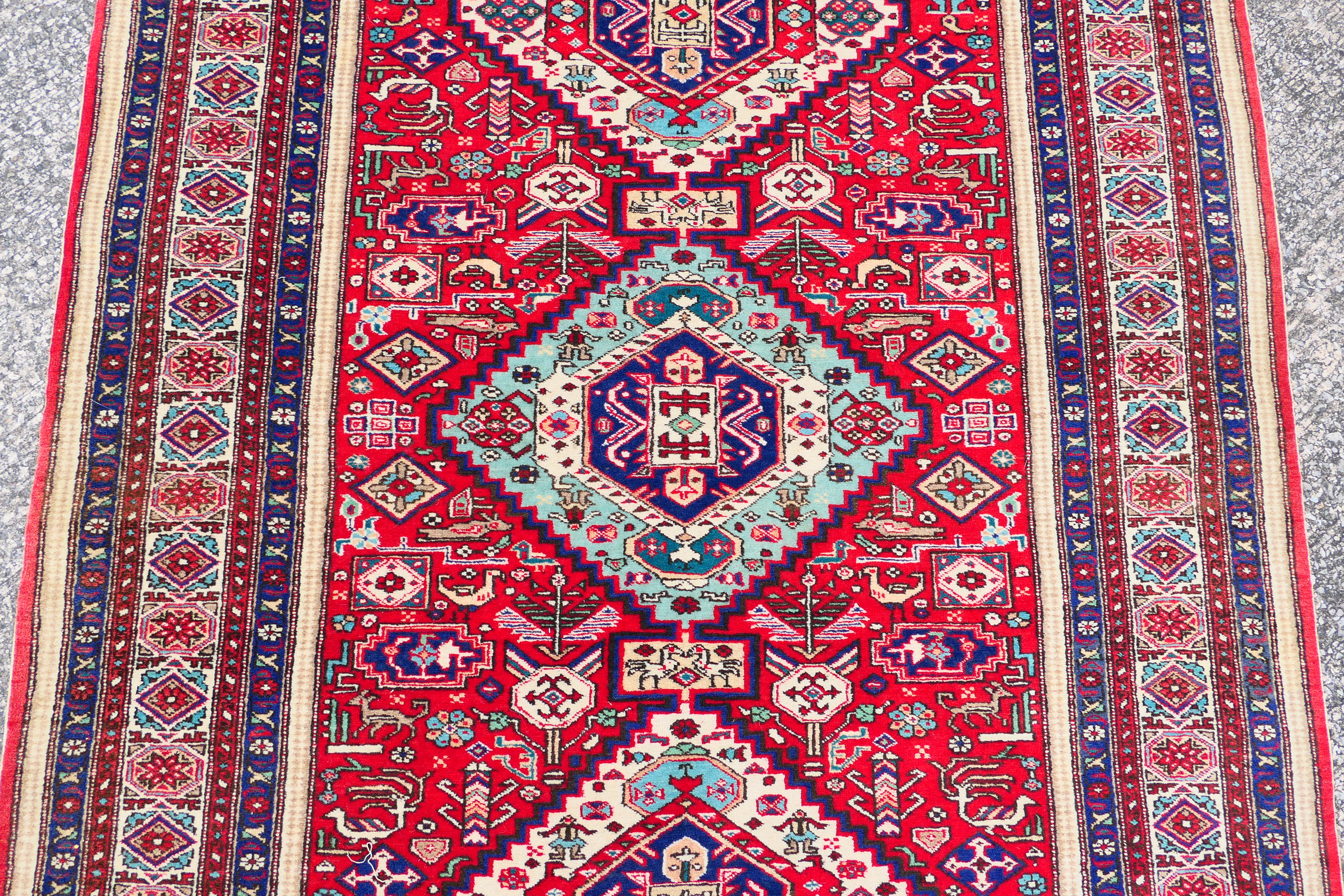 A Persian rug with triple lozenge medallions on a red ground within repeating border, - Image 3 of 5