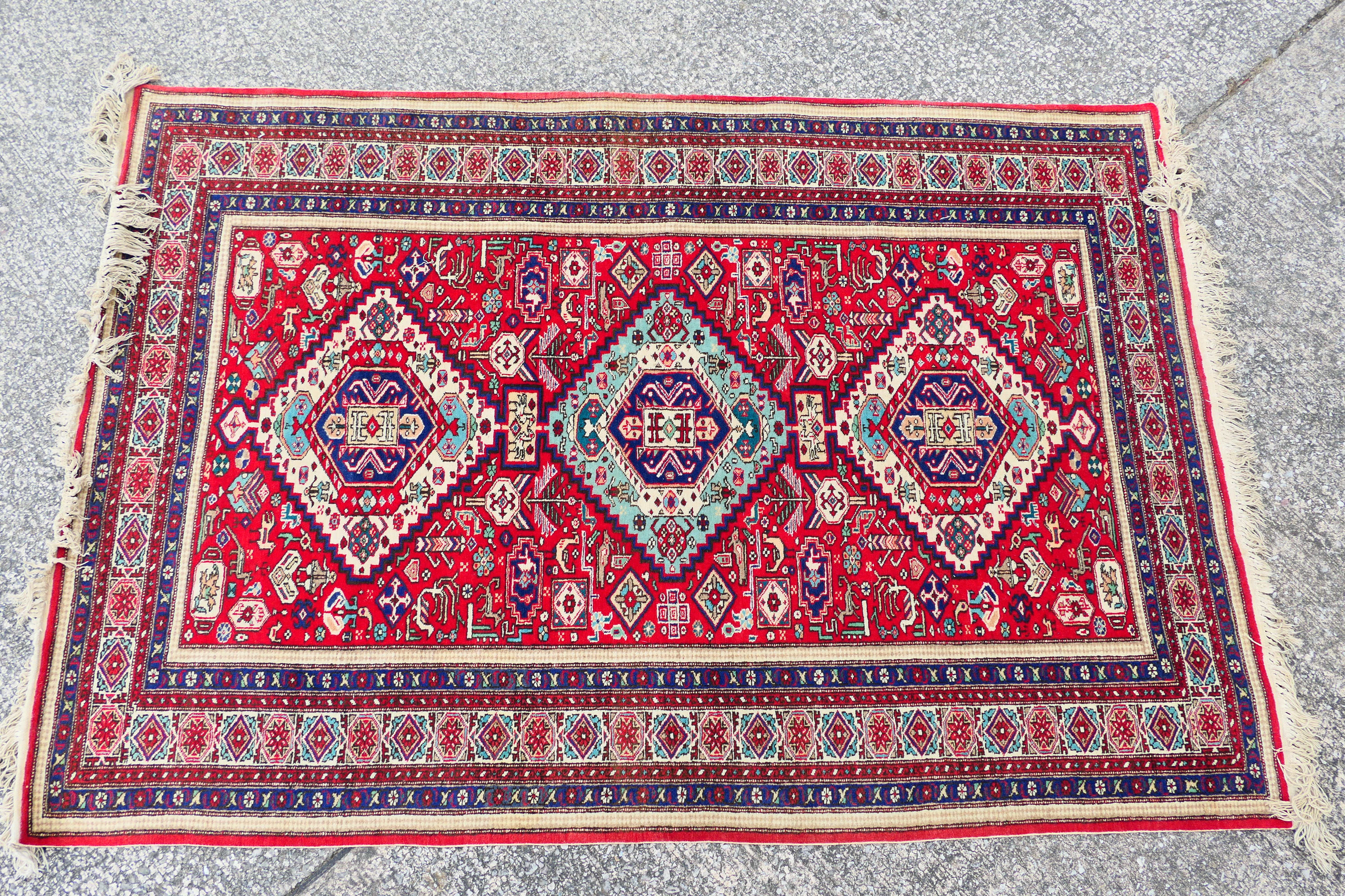 A Persian rug with triple lozenge medallions on a red ground within repeating border,