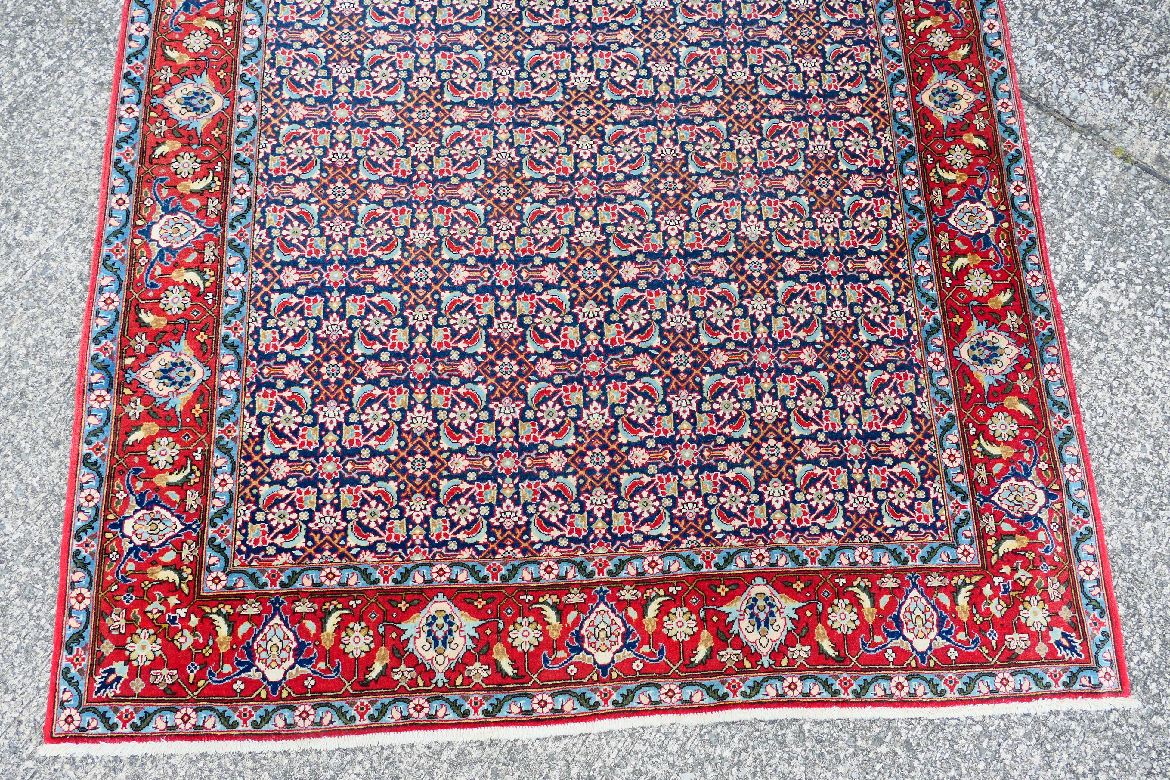 A Persian rug with central blue field with all over polychrome floral decoration within repeating - Image 2 of 6
