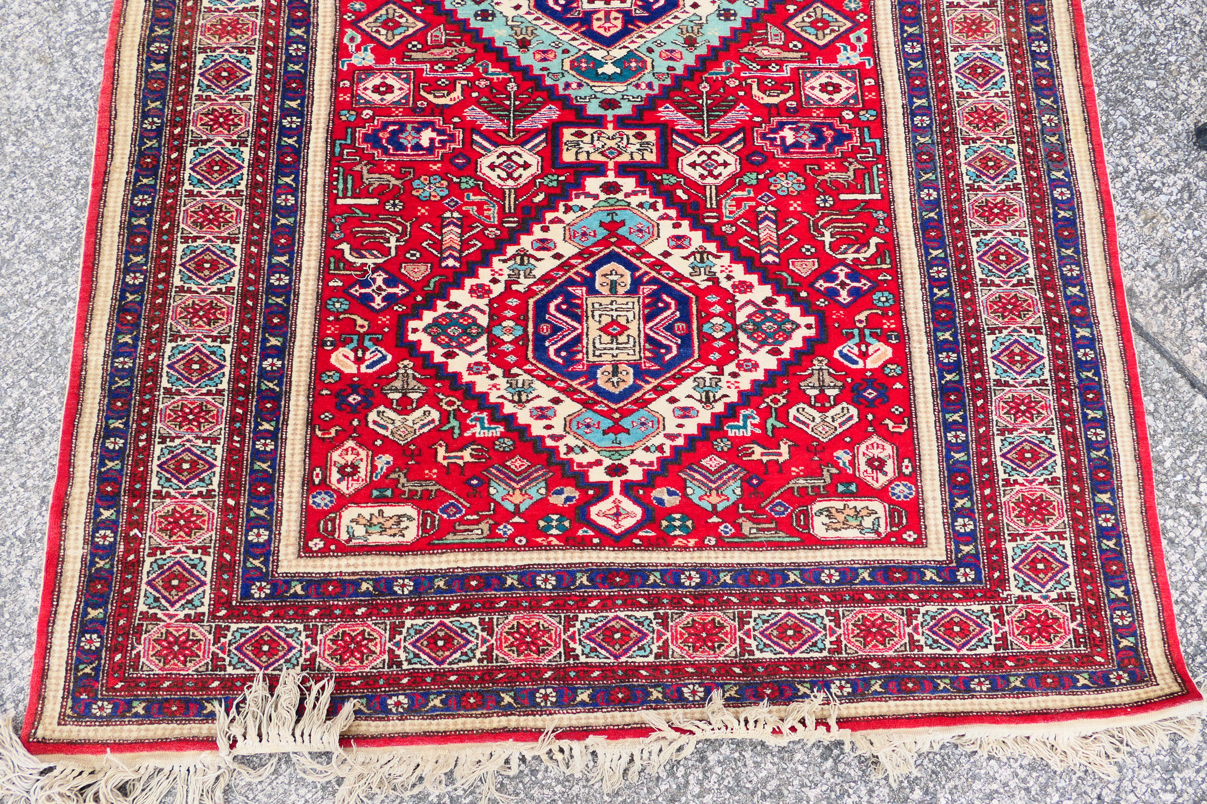 A Persian rug with triple lozenge medallions on a red ground within repeating border, - Image 2 of 5