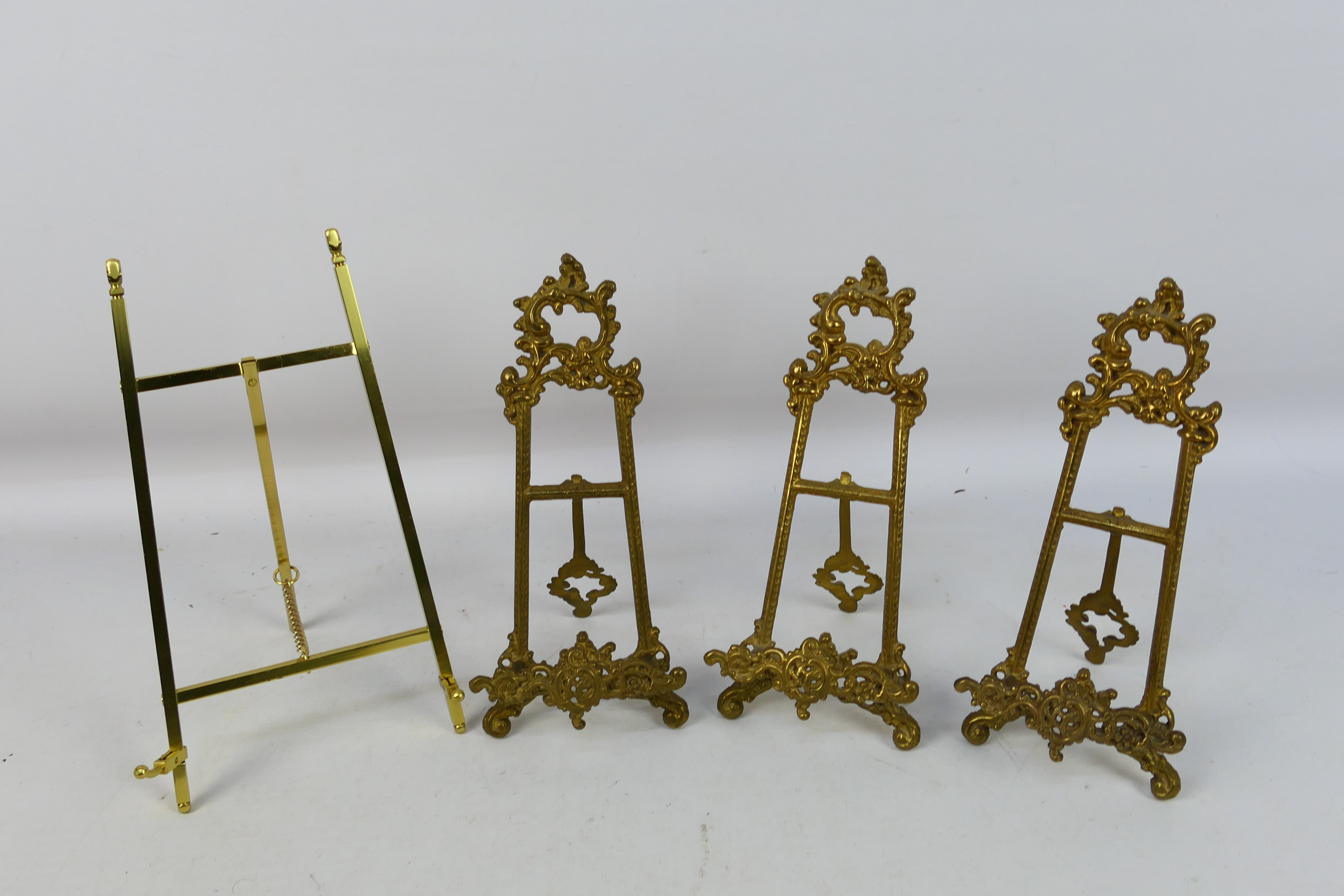 Three cast brass, easel plate stands and one similar.