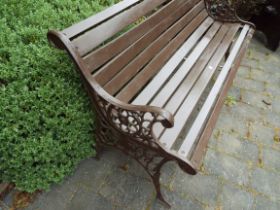 A two seat garden bench with slatted seat and combined back raised on cast iron scroll pattern