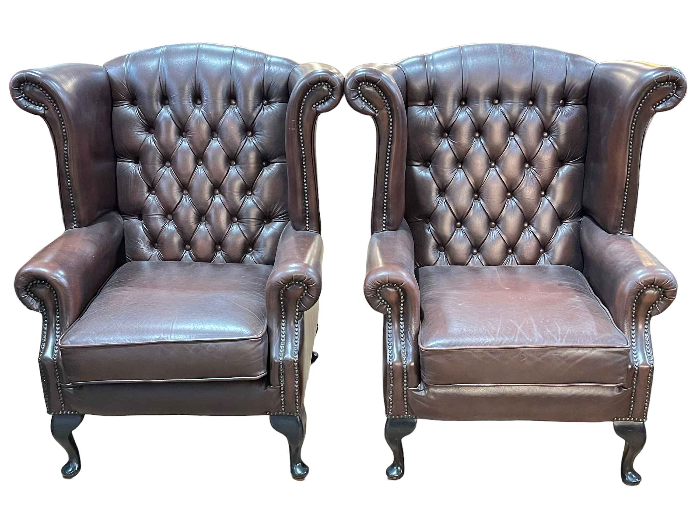 Pair Thomas Lloyd brown deep buttoned leather and studded wing armchairs.