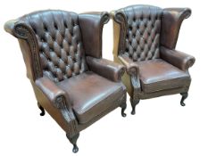 Pair Thomas Lloyd brown deep buttoned leather and studded wing armchairs.