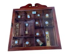 Collection of miniature brass clocks in wall mounted display case.