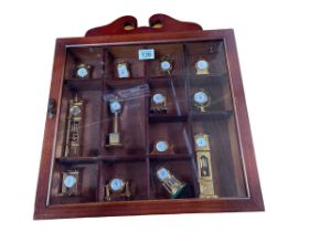 Collection of miniature brass clocks in wall mounted display case.