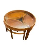 Circular glass topped teak coffee table with three oval nesting tables below.