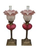 Pair of small brass oil lamps with ruby glass reservoirs and tinted pink frosted shades, 44cm.