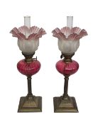 Pair of small brass oil lamps with ruby glass reservoirs and tinted pink frosted shades, 44cm.