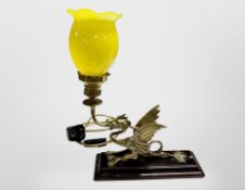 A brass table lamp in the form of a dragon on lacquered plinth with yellow glass shade,