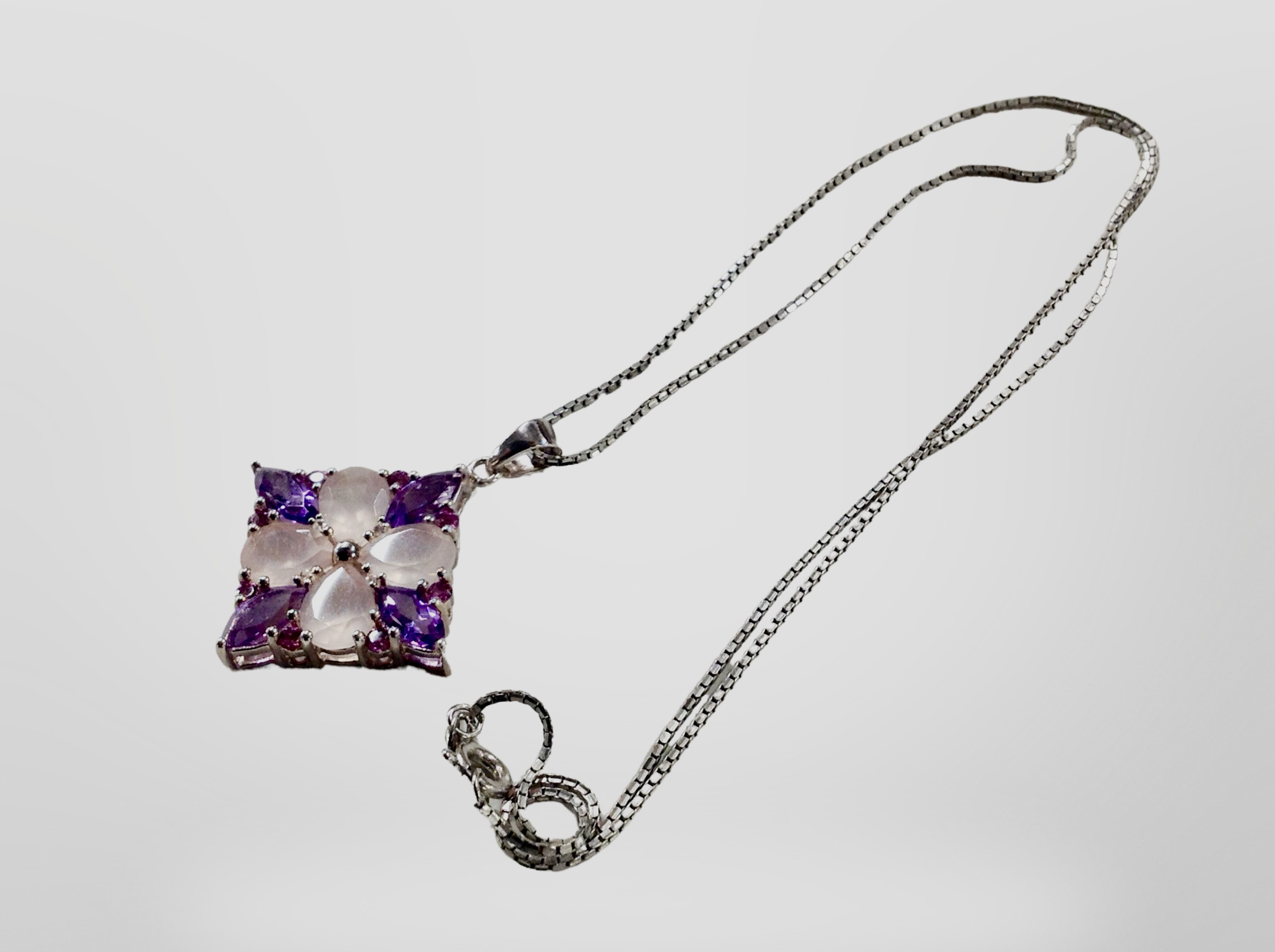 A silver pendant on chain set with pink and amethyst coloured stones