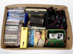 A box of Blu-ray discs, PS3 games, CDs, vintage cameras, radio.