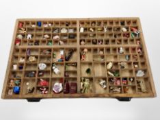 A printer's type tray containing assorted trinkets, china thimbles, ornaments, etc.