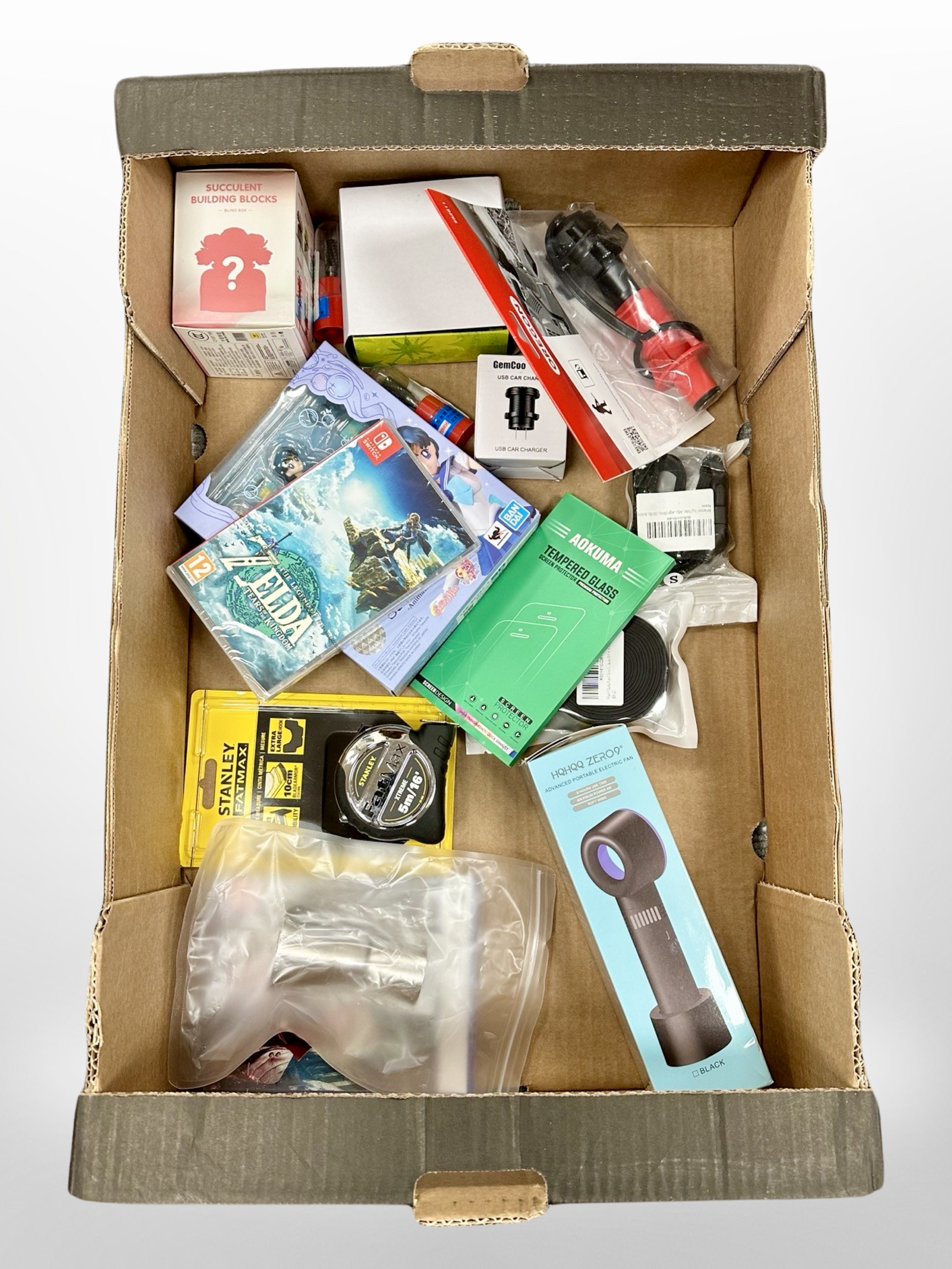 A box of new retail stock items - tape measure, Nintendo Switch game, PS5 game,