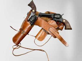 A pair of non-working single-action army revolvers with leather holster belt.