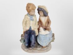 A Nao figure of a boy and girl sat on a tree trunk.