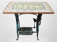 A cast iron sewing machine table base on castors with later mosaic tiled top,