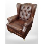 A contemporary brown leather wing back armchair on brass castors
