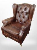 A contemporary brown leather wing back armchair on brass castors