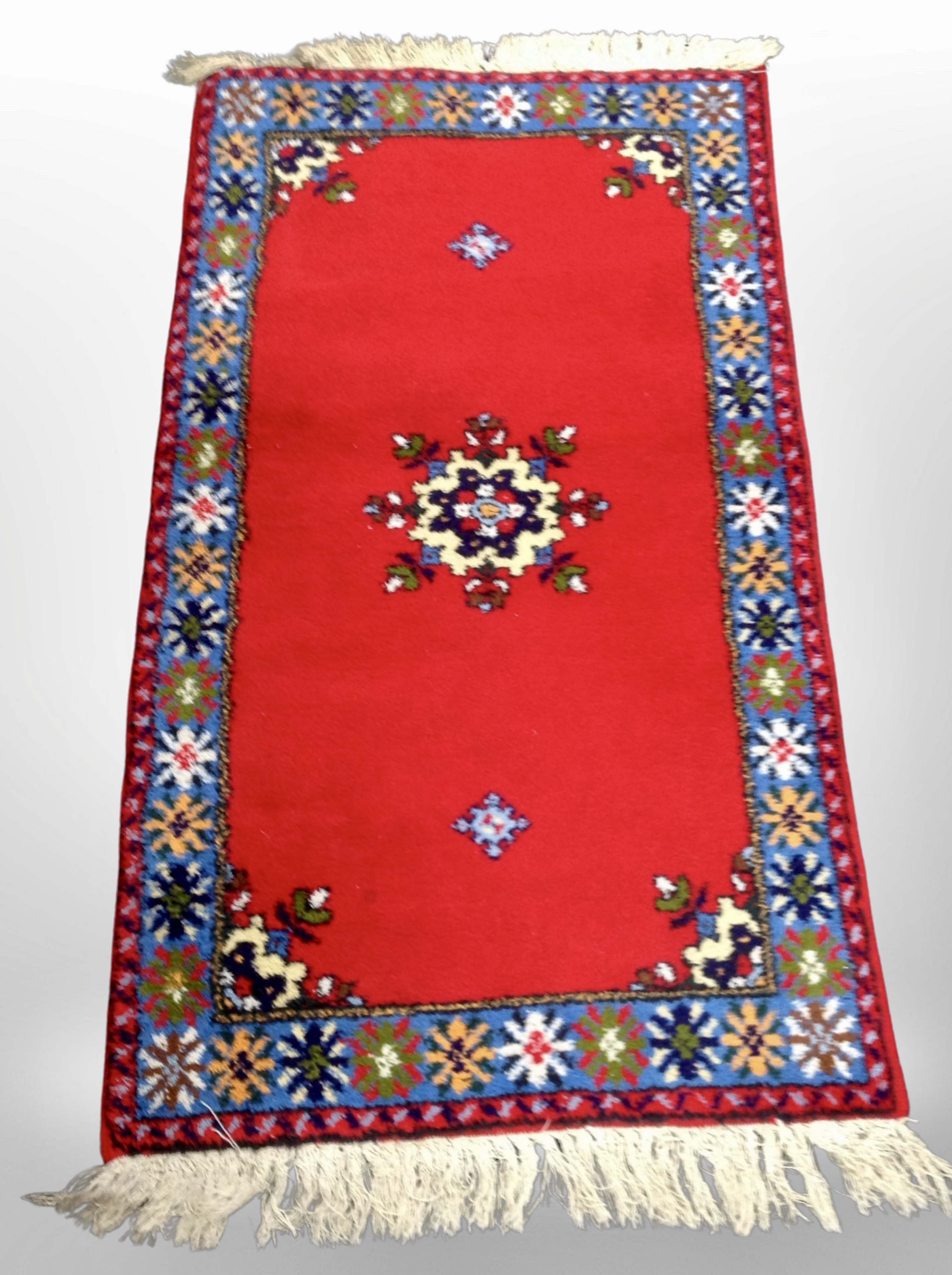 An Eastern woolen rug on red ground, 160cm x 83cm.