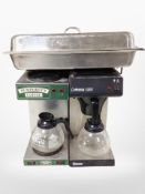 Two commercial stainless steel coffee makers and a lidded catering tray