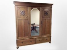 An Edwardian oak triple wardrobe with central mirrored door, raised on bun feet,
