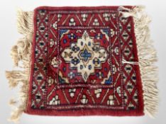 A small Iranian fringed mat on red ground, 39cm x 32cm.