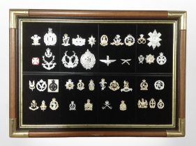 A montage of reproduction cap badges in brass-mounted frame, 69cm x 50cm overall.