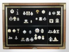 A montage of reproduction cap badges in brass-mounted frame, 69cm x 50cm overall.