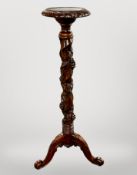 A heavily carved hardwood torchere on scroll tripod base,
