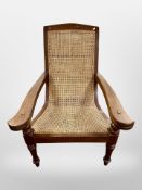 An early 20th century teak and bergere plantation armchair with fold-out arm rests,