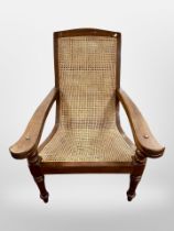 An early 20th century teak and bergere plantation armchair with fold-out arm rests,