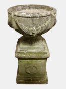 A weathered concrete garden urn on plinth,