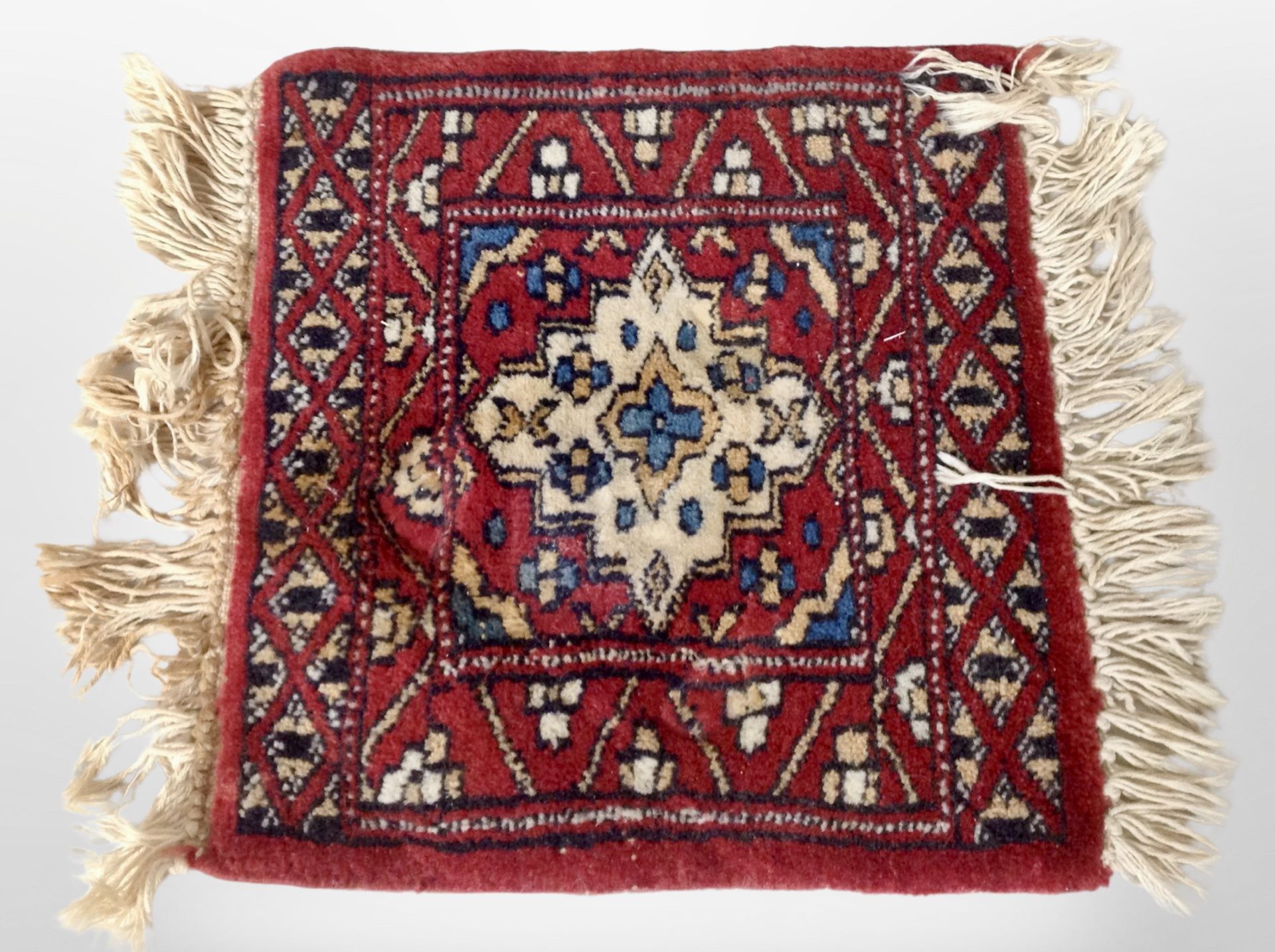 A small Iranian fringed mat on red ground, 39cm x 32cm.