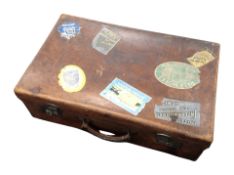 An early 20th century stitched brown leather luggage case with various shipping labels,