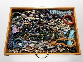 A wooden drawer containing assorted costume jewellery, bead necklaces, bracelets, etc.