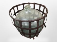 A wrought-metal basket containing a glass carboy, height 52cm.